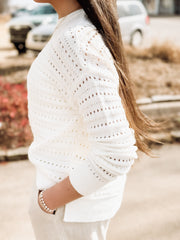 Person wearing a white lace top with a blurred outdoor background
