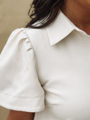 Close-up of a person wearing a cream dress with short sleeves.