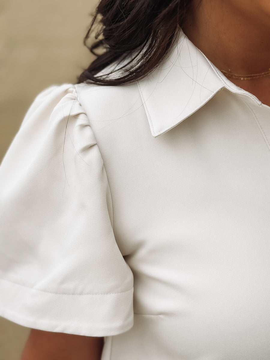 Close-up of a person wearing a cream dress with short sleeves.