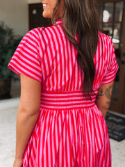 Woman in a pink and red striped dress standing next to a potted plant with pink flowers.