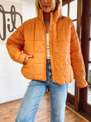 Person wearing an orange puffer jacket and blue jeans indoors.