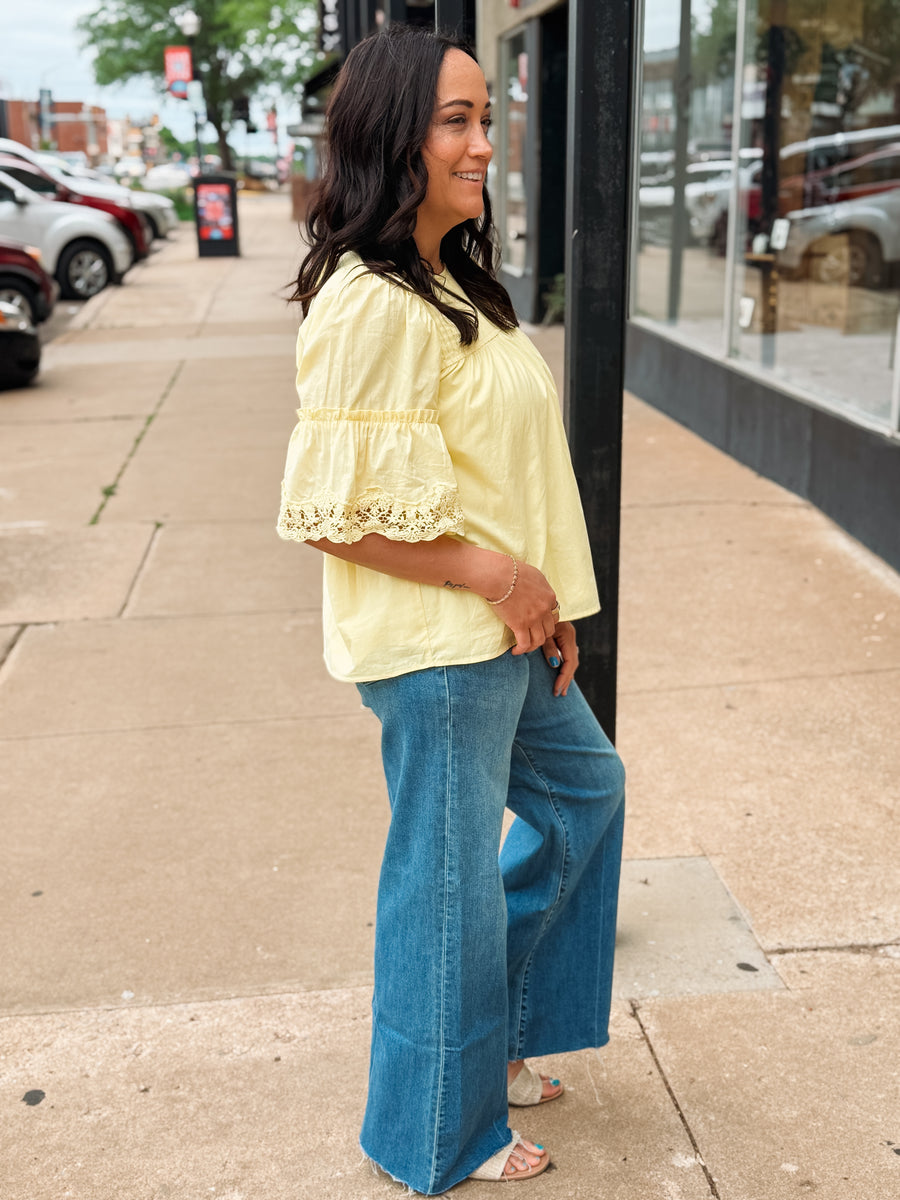 Woman wearing a yellow blouse and blue jeans standing on a sidewalk.
